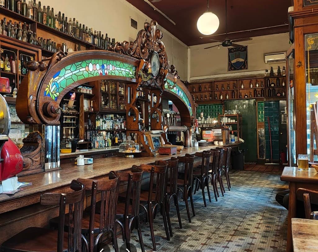Interior del Bar El Federal con barra art nouveau de roble tallado, vitrales y sillas bistró sobre mosaicos antiguos