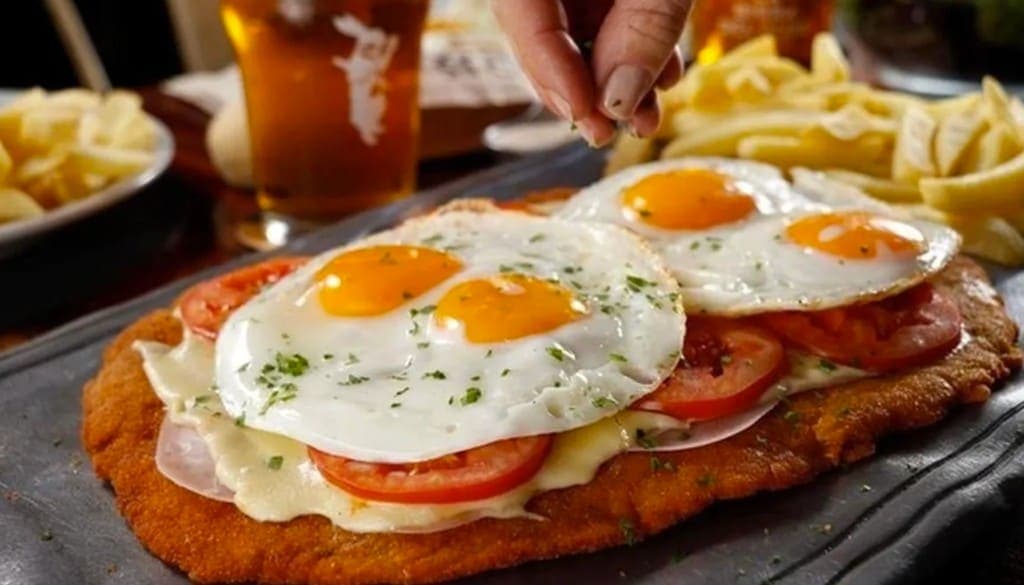 Milanesa napolitana con huevos fritos, papas y cerveza en un bodegón porteño