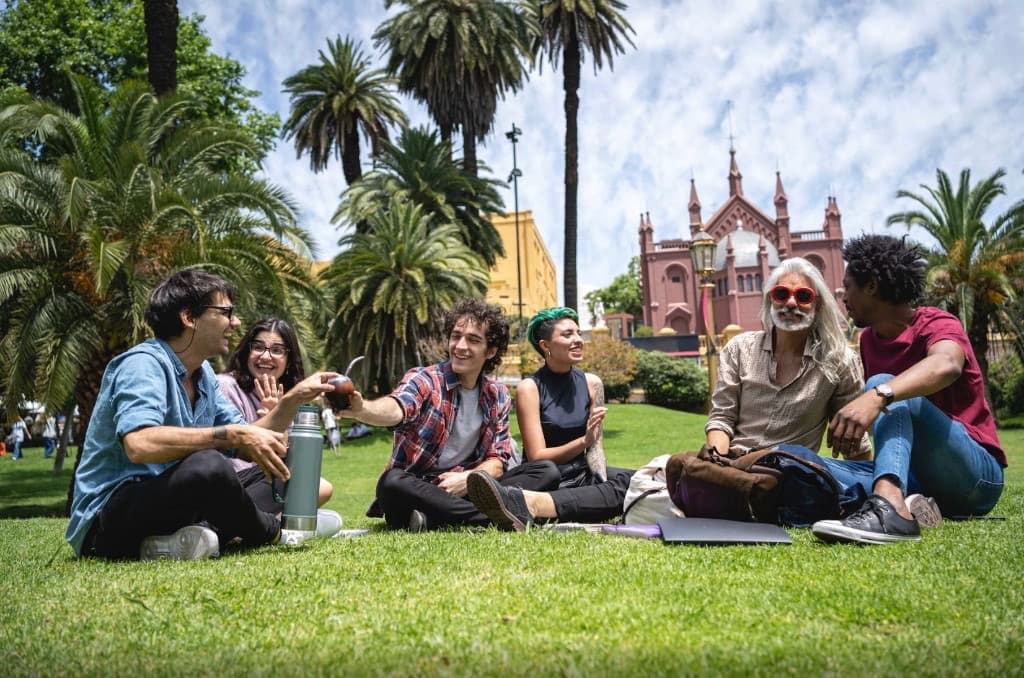 Grupo de amigos compartiendo mate en el pasto entre palmeras de Plaza Francia