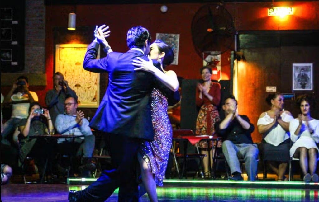Pareja bailando tango frente al público que aplaude en una milonga porteña